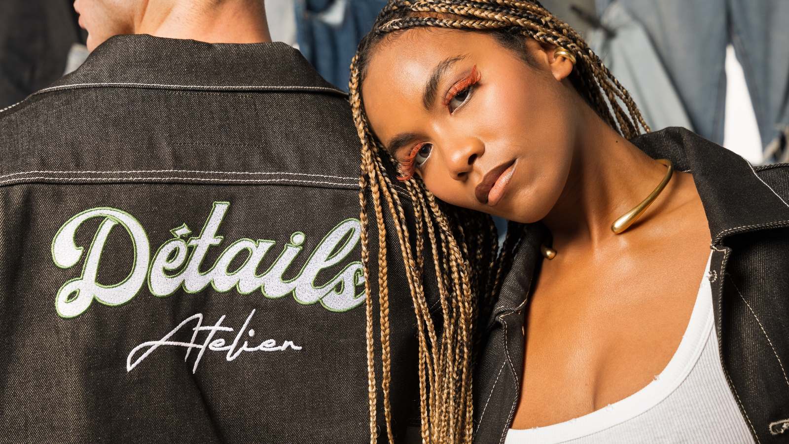 The Détails Atelier script embroidered across the back of a jacket, the second model resting against the shoulder
