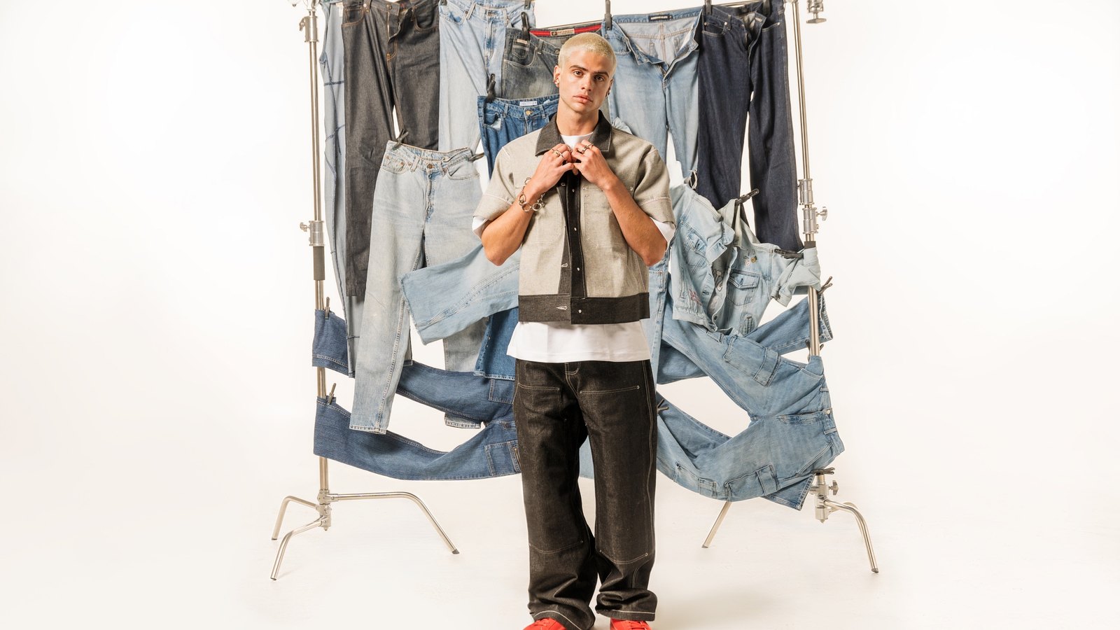 A model in a raw denim shirt stands in front of the backdrop built from secondhand jeans, the C-stands holding it up left visible in frame