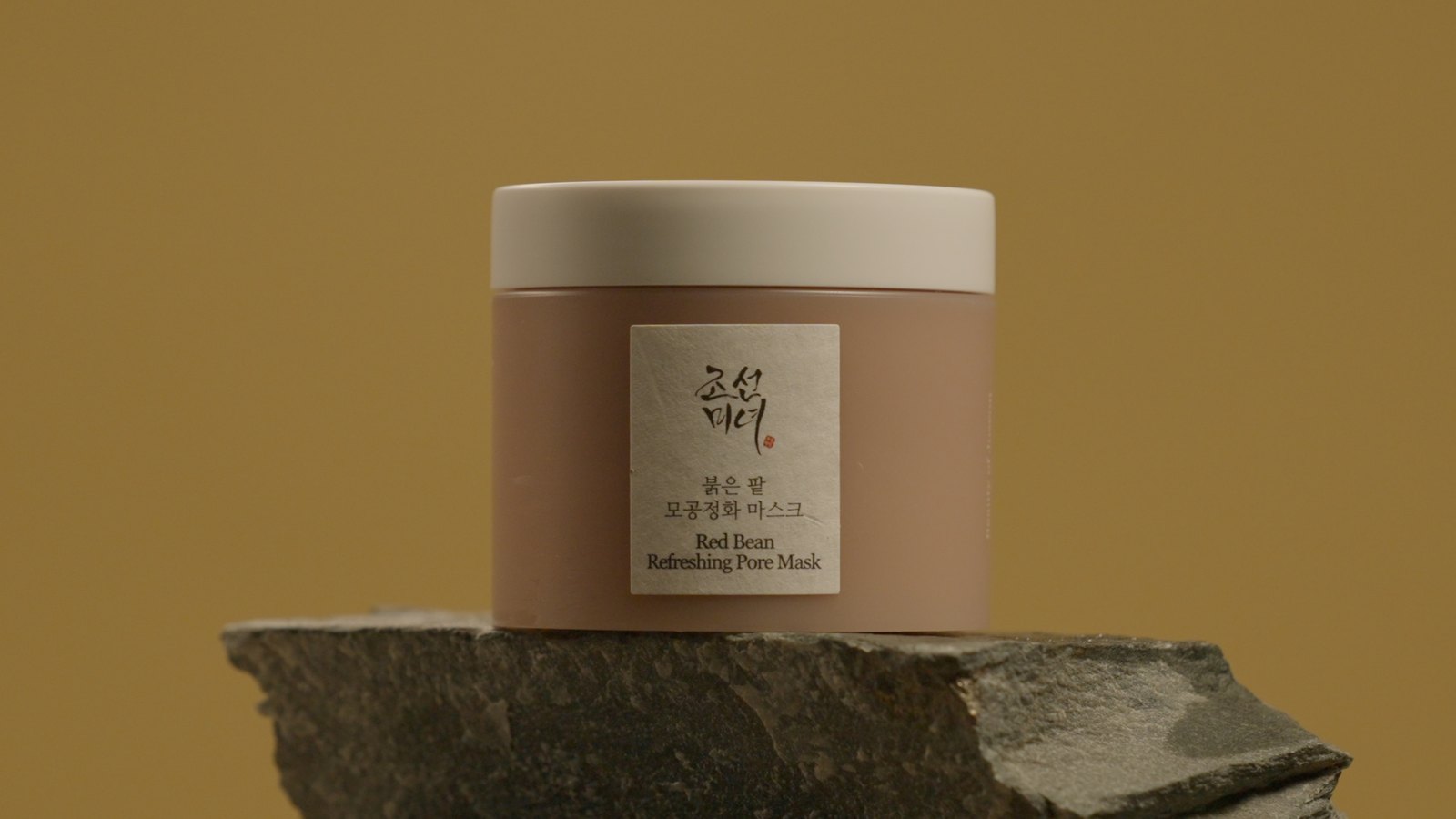 The jar on wet slate against the olive-ochre backdrop, the hero product frame