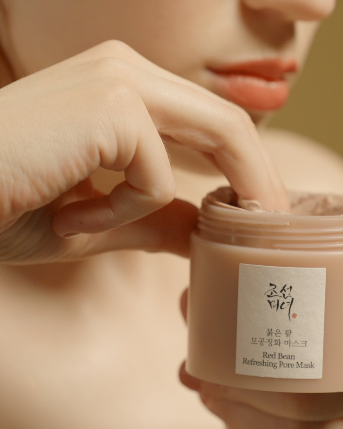 Fingers reaching into the open jar of clay mask