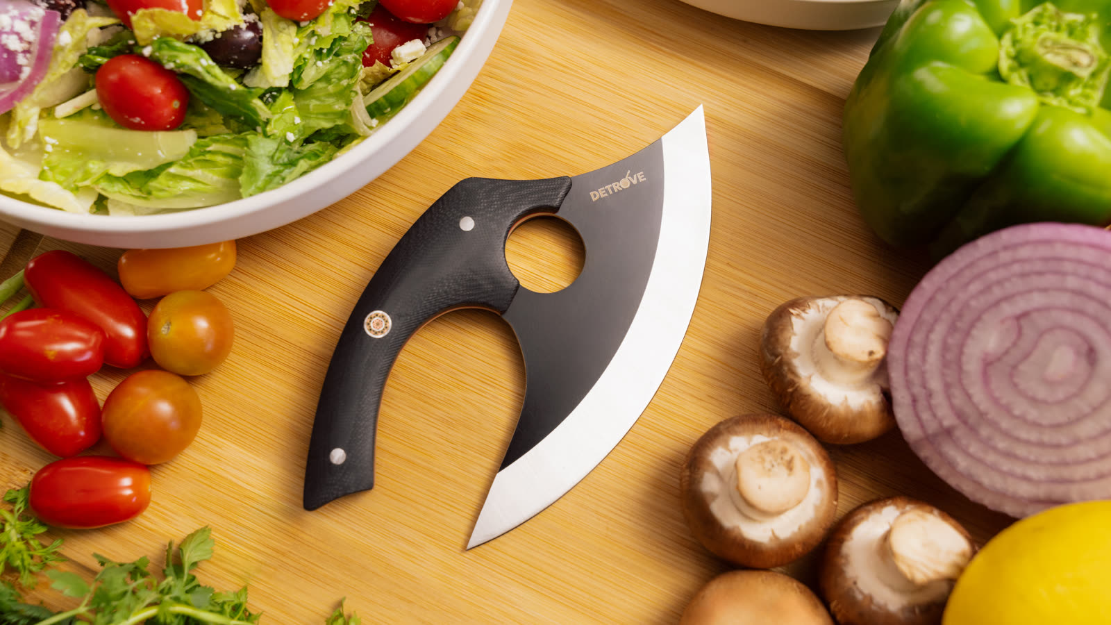 The blade on a bamboo board, surrounded by a dressed salad, tomatoes, mushrooms, red onion and a green pepper