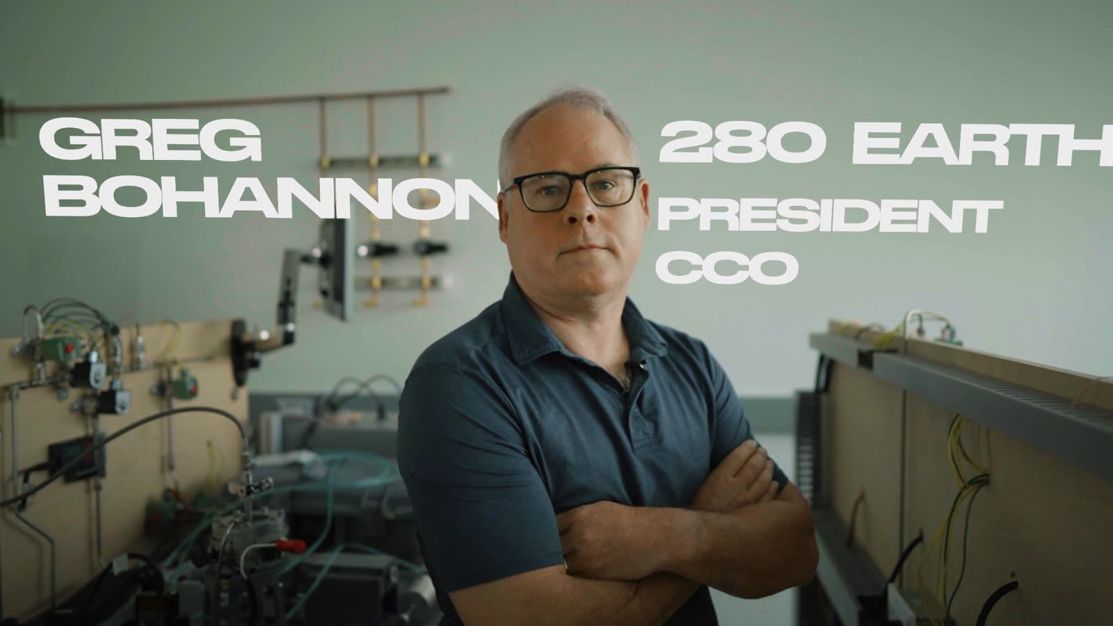 Greg Bohannon stands with his arms crossed beside the test rigs at 280 Earth’s headquarters, his name and title set beside him