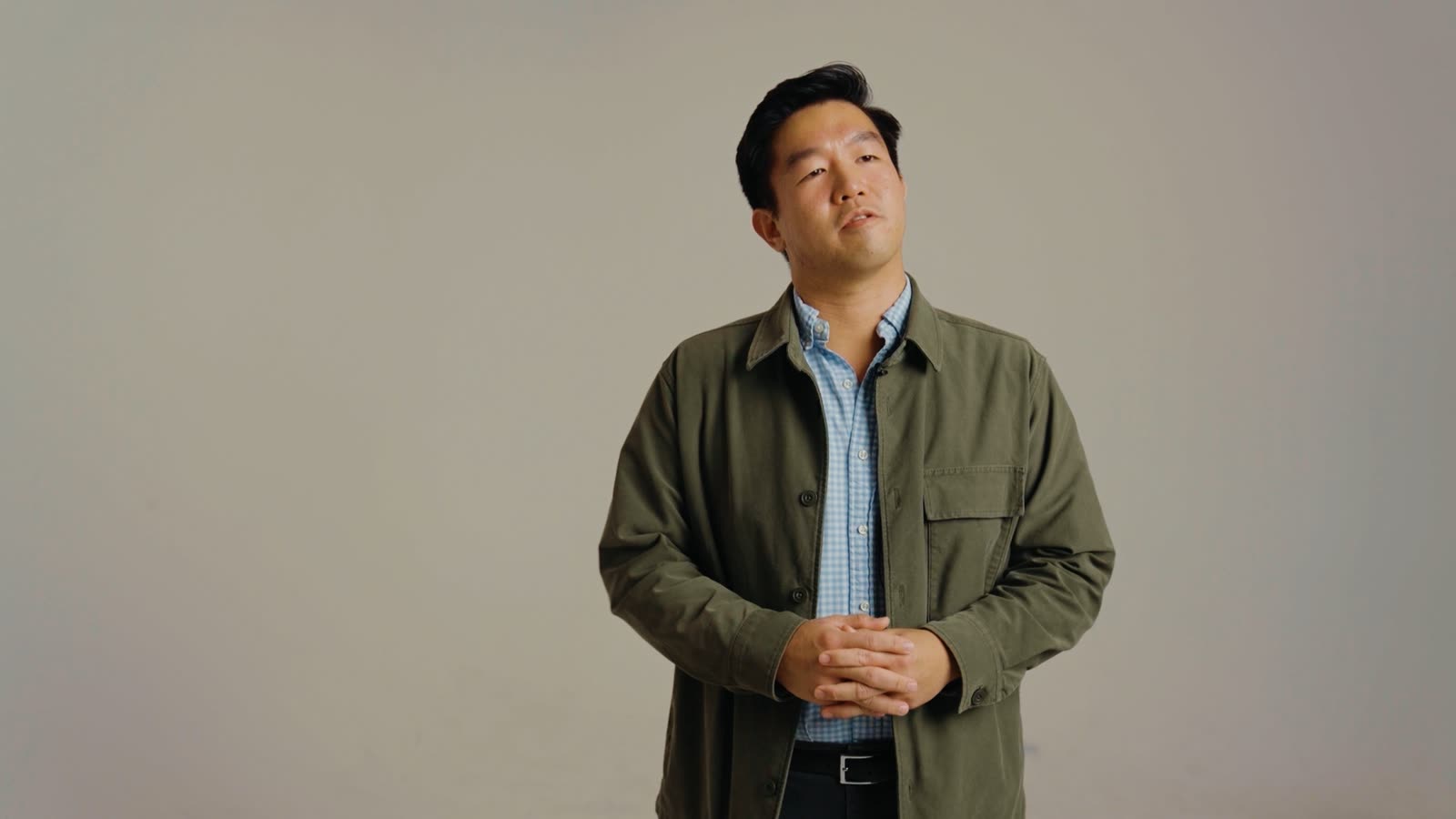 Euweng Chan stands with his hands clasped on a plain backdrop, framed from the waist up