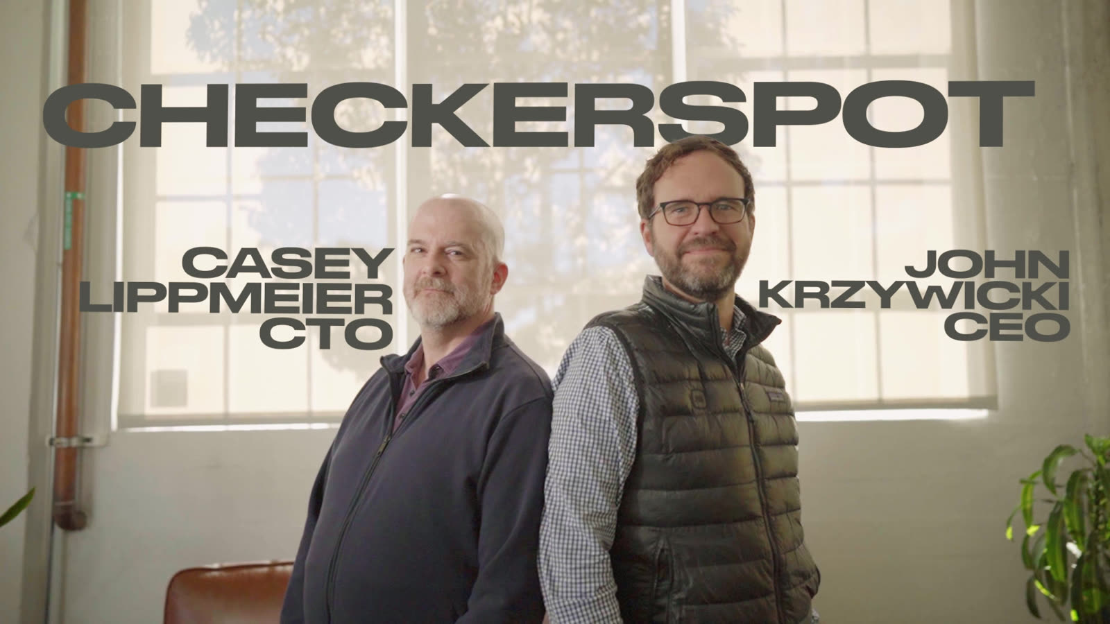 Casey Lippmeier and John Krzywicki stand back to back in the daylit Checkerspot lab, their names and titles set beside them