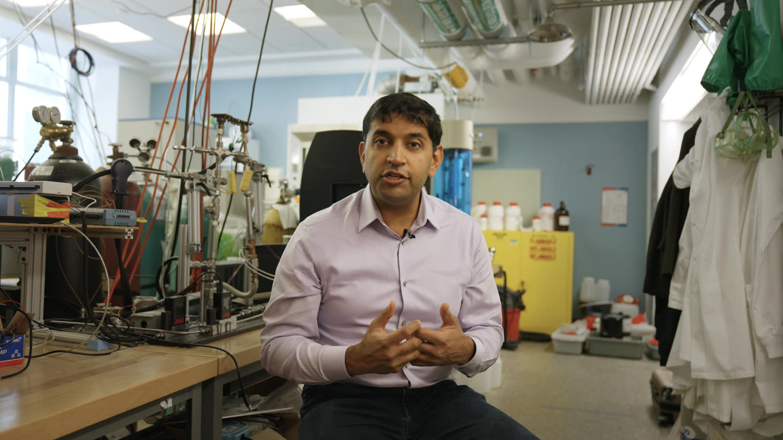 Anurag Bajpayee speaks with his hands steepled, seated in a working Gradiant lab among test rigs and gas lines