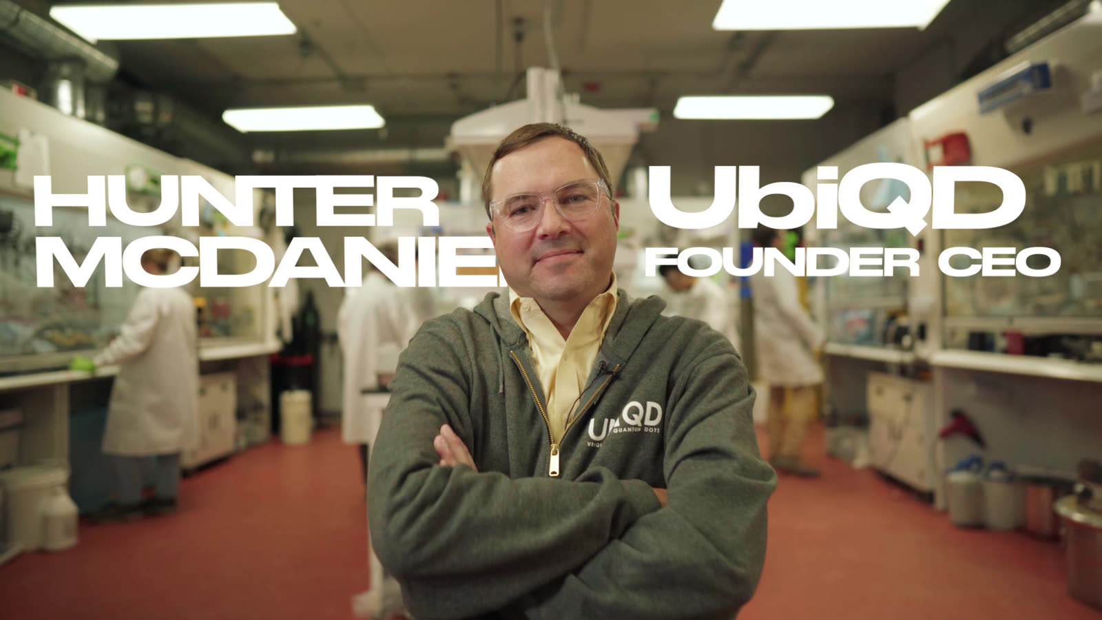 Hunter McDaniel stands with his arms crossed on the UbiQD lab floor, his name and title set beside him