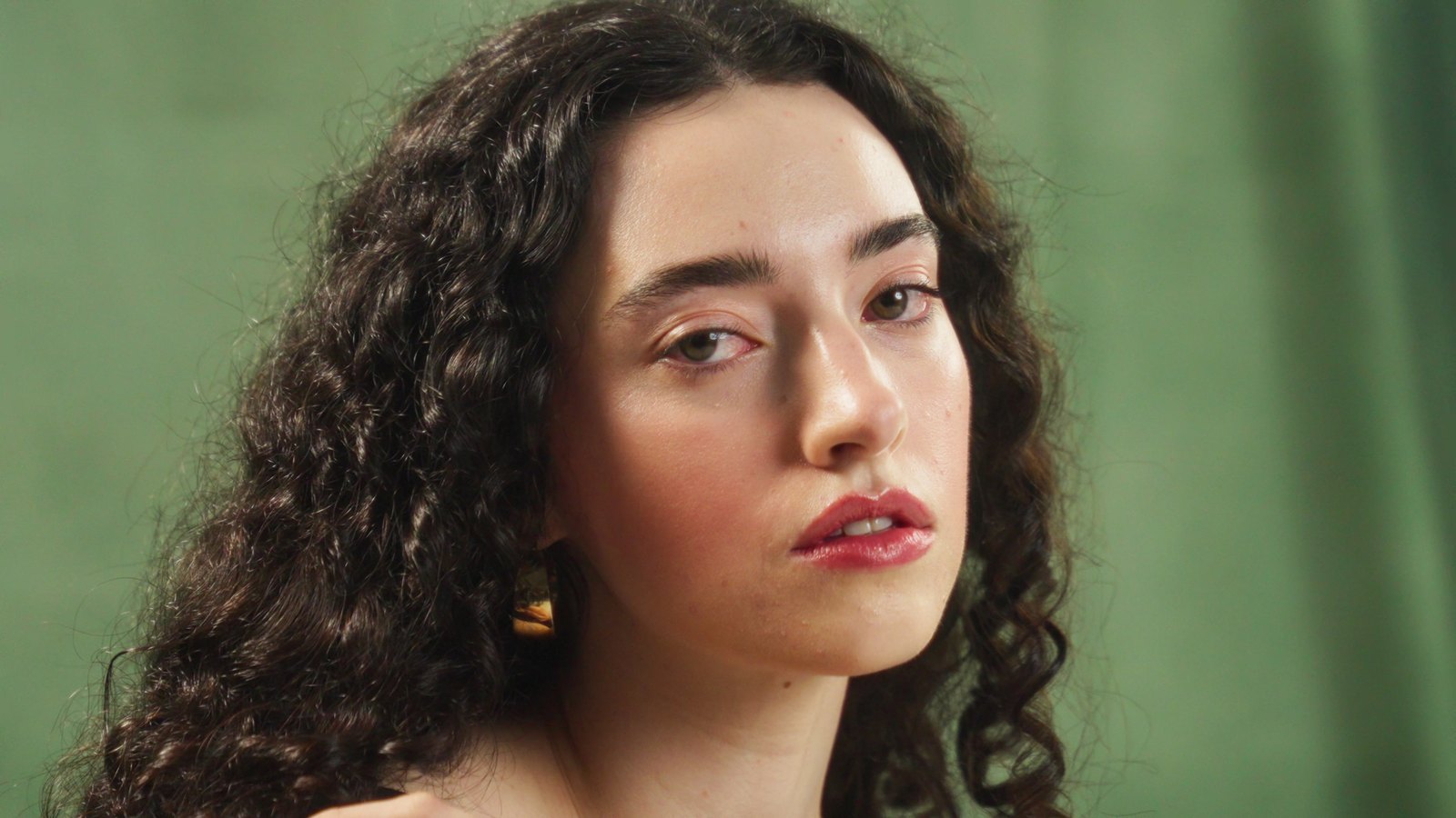 Close portrait, direct to camera, against the hand-painted olive backdrop
