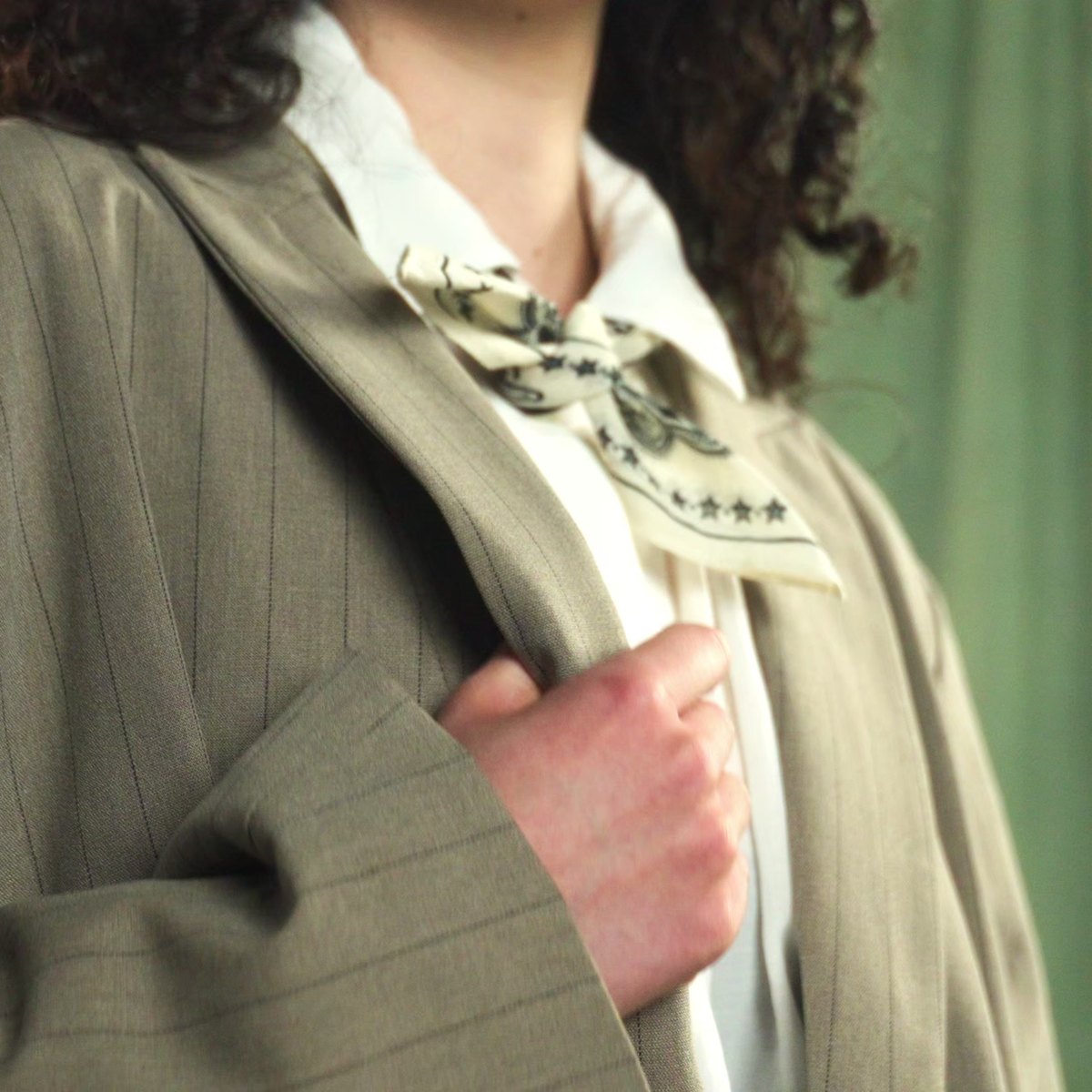 Detail of the neck scarf tied like a cravat against the olive backdrop