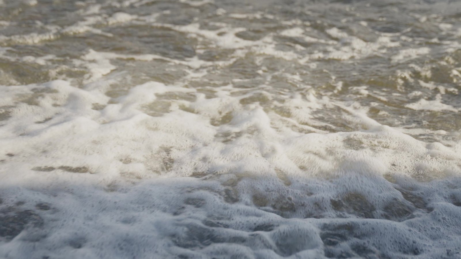 Abstract texture frame of surf foam breaking over sand at golden hour